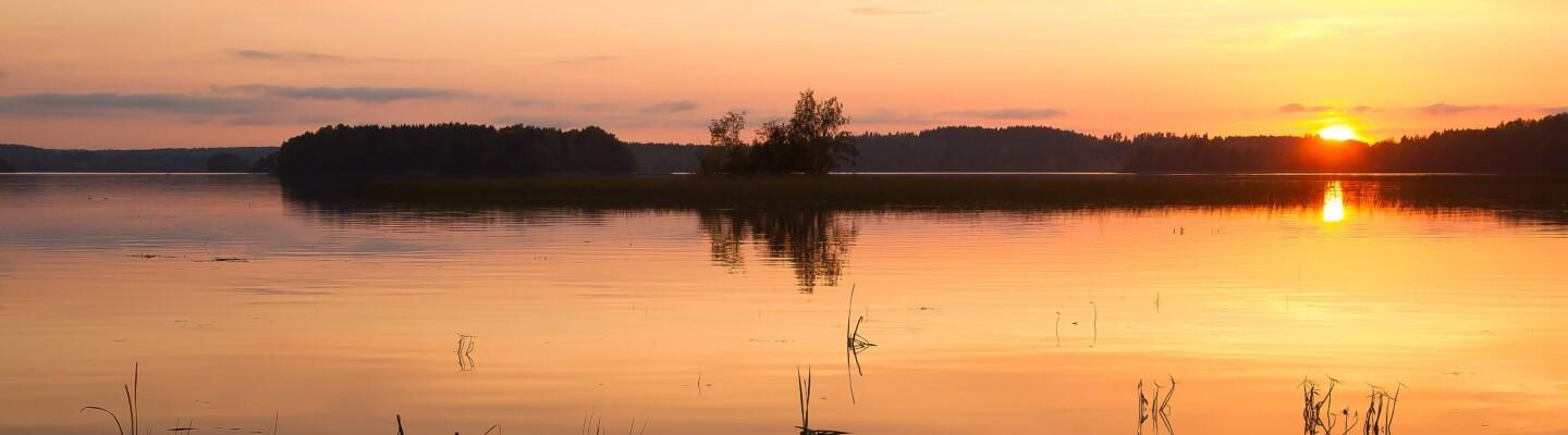Kesäinen kuva järvimaisemasta, jossa aurinko laskee