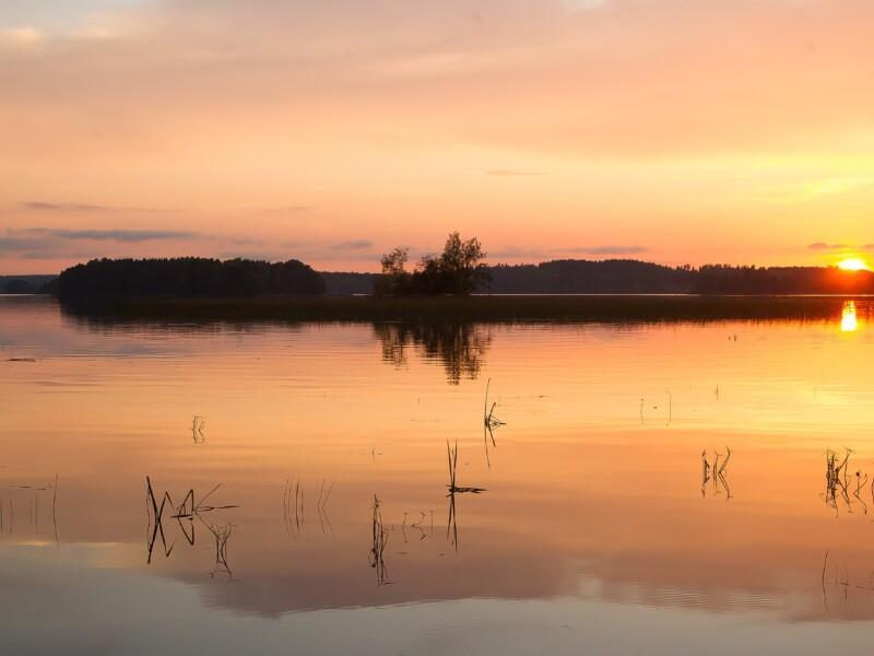 Kesäinen kuva järvimaisemasta, jossa aurinko laskee
