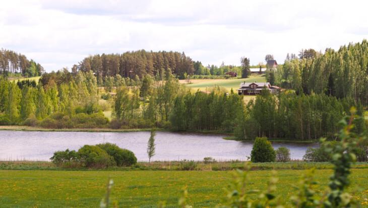 Kuva maalaismaisemasta, jossa näkyy peltoa, vesistöä ja talo